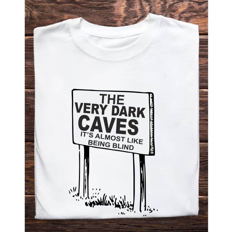 Father Ted Themed "Very Dark Caves" T-Shirt from Joke.ie, Ireland. Step into the hilariously absurd world of Father Ted with our exclusive Very Dark Caves Tee Shirt, inspired by one of the most memorable moments from the beloved comedy series. This t-shirt is perfect for fans who appreciate the quirky humor and iconic scenes that have made Father Ted a timeless classic. Design and Style The Very Dark Caves Tee Shirt features a whimsical illustration of a signpost pointing towards the "Very Dark Caves," a nod to the show's famous episode where the characters encounter the hilariously named attraction. The signpost is depicted in a charming, cartoonish style, capturing the essence of Father Ted's humor. The background subtly incorporates elements of the Craggy Island landscape, adding an extra layer of nostalgia for dedicated fans. Material and Comfort Made from high-quality cotton, this t-shirt offers superior comfort and durability. The fabric is soft to the touch, ensuring a cozy fit whether you're lounging at home, out for a casual day, or attending a themed event. The material is pre-shrunk, so the shirt maintains its shape and fit wash after wash, making it a reliable addition to your wardrobe. Nostalgic and Humorous Wearing the "Dark Cave" T-Shirt is a delightful way to celebrate the unique humor of Father Ted. The design instantly evokes memories of the show's funniest moments, bringing a smile to anyone who recognizes the reference. It's a subtle yet effective way to showcase your love for the series and connect with other fans. Versatile and Stylish This t-shirt is as versatile as it is stylish. Pair it with jeans, shorts, or even pajama bottoms for a comfortable and casual look. Its classic fit makes it suitable for any occasion, whether you're heading to a comedy show, hanging out with friends, or simply relaxing at home. Perfect Gift for Fans Looking for a perfect gift for a Father Ted enthusiast? The "Dark Cave" T-Shirt is an excellent choice. Its unique design and high-quality construction make it a thoughtful and enjoyable present for birthdays, holidays, or any special occasion. Celebrate the humor and nostalgia of Father Ted with the "Dark Cave" T-Shirt. Featuring the iconic signpost pointing to "The Very Dark Caves," this shirt is a must-have for any fan of the show. Enjoy the comfort of premium cotton and the joy of sharing your favorite TV moments with the world. Get your "Dark Cave" T-Shirt today and add a touch of Craggy Island charm to your wardrobe! Colour: White loose fit tee Size: Small 35/37″ Medium 38/40″ Large 41/43″ X Large 44/46″ 2X Large 47/49″ 3X Large 50/522 View our entire Father Ted Collection here.